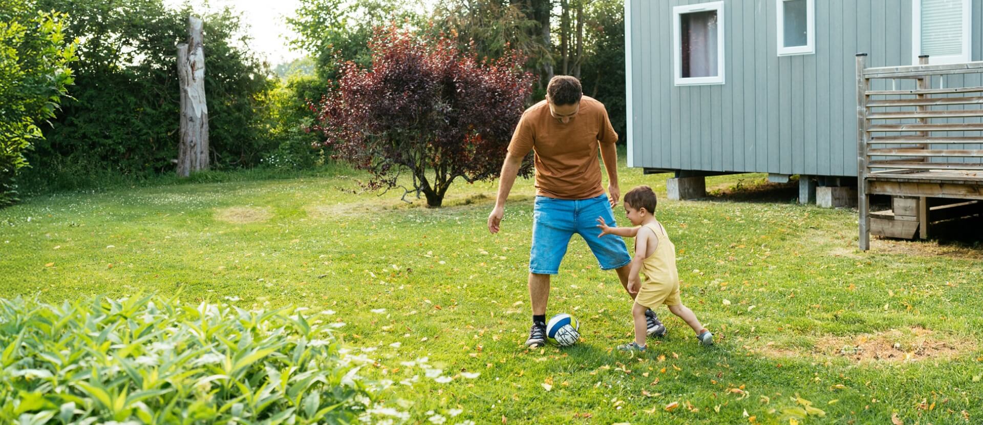 Young son and father playing soccer in their yard